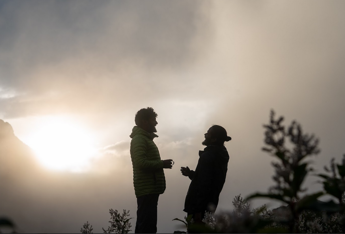 People sharing herbal infusion outdoors at mountain camp during early morning light