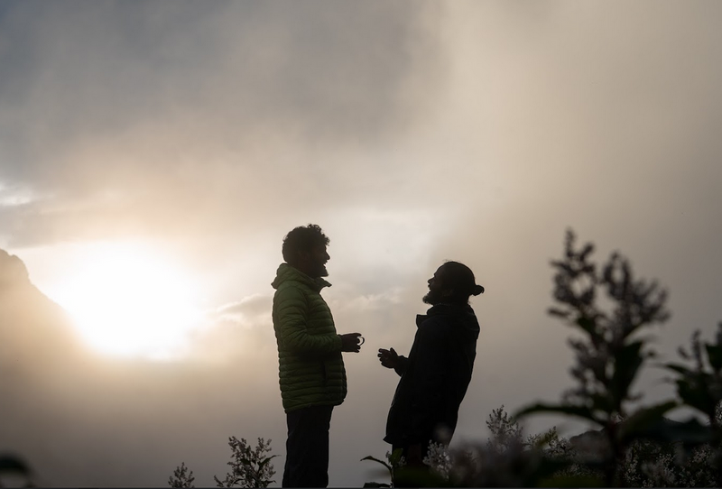 People sharing herbal infusion outdoors at mountain camp during early morning light
